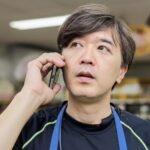 紺色のTシャツに青いエプロンを着けている店主が、コールセンターに電話をかけている様子